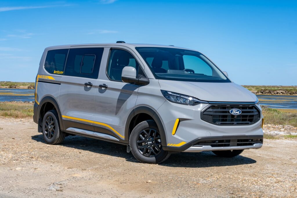 Ford Custom Trail gris Aventourer de T&T Vans avec accents jaunes, stationné en bord de mer et exposé au salon des vans