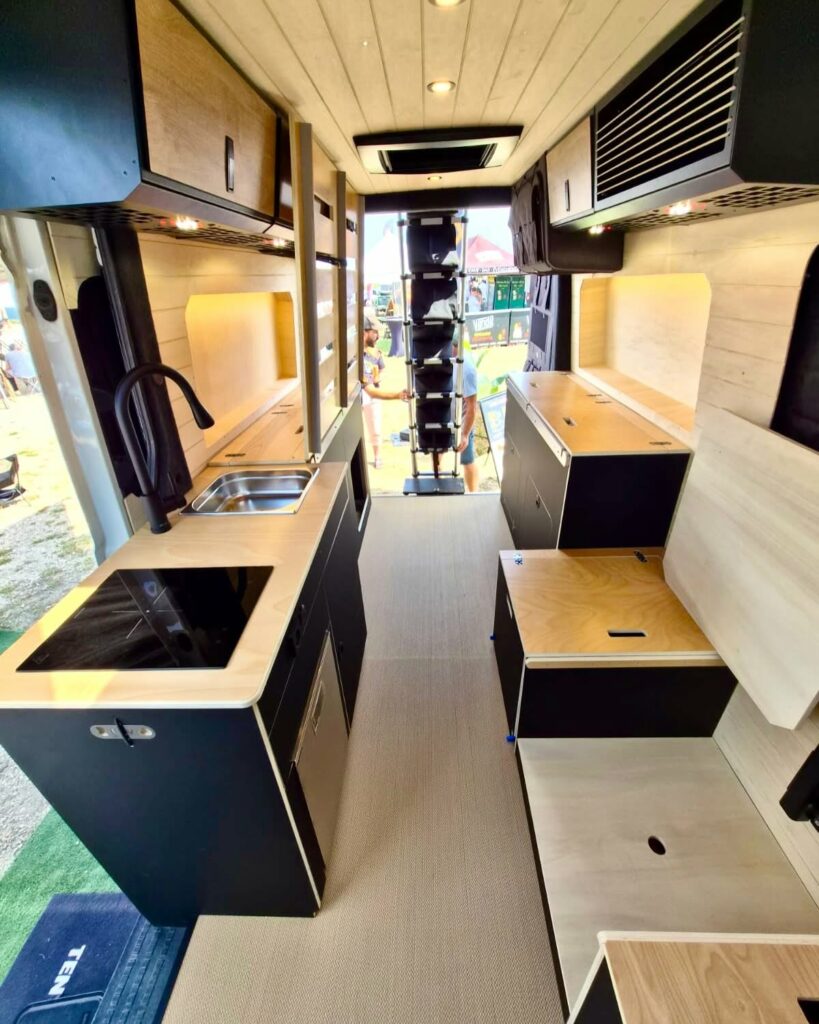Aménagement complet de van avec cuisine, évier et rangements bois et noir, kit FLV Van présenté sur un salon vanlife