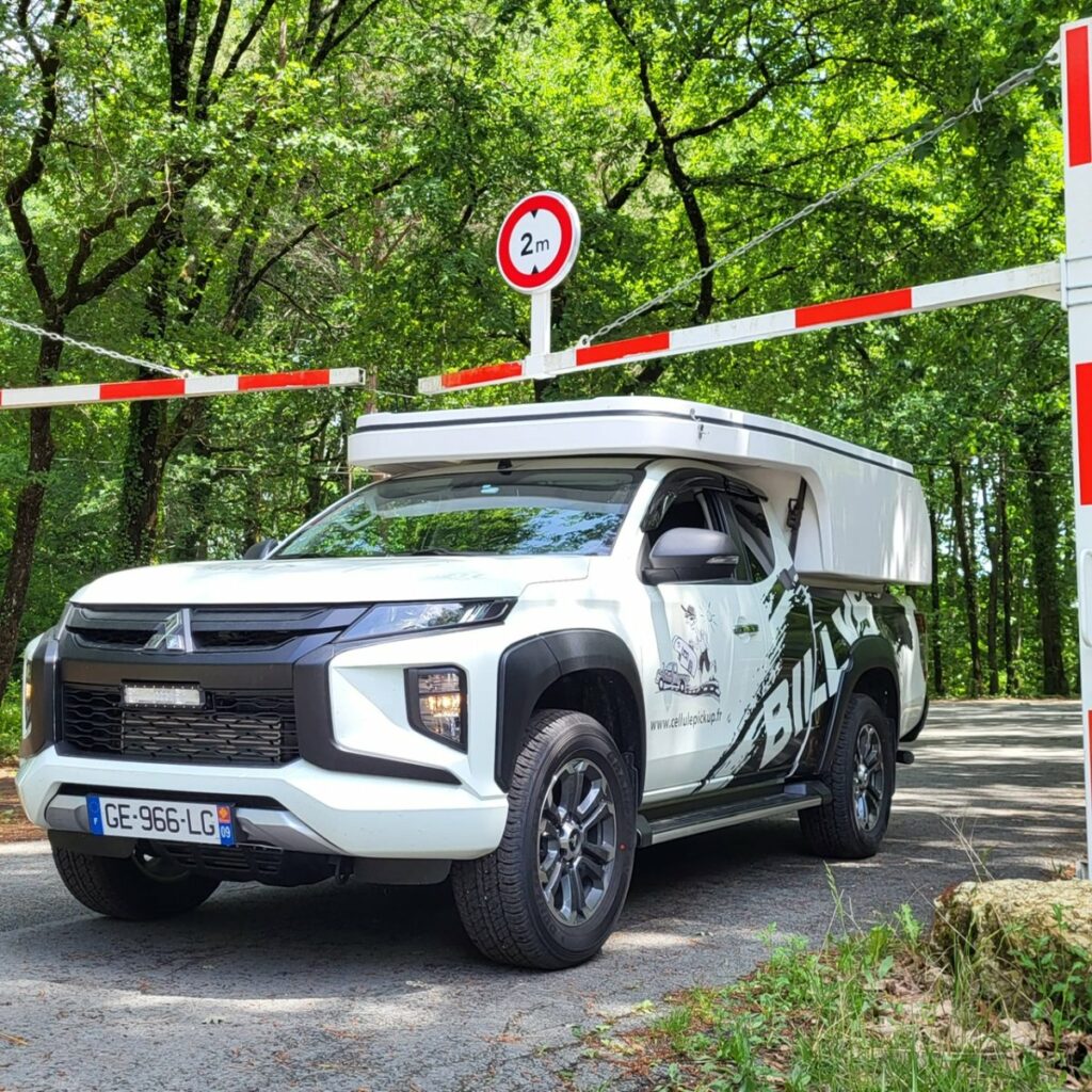 Pick-up Mitsubishi équipé d'une cellule Billys fermée, floqué "Bivouac" au passage d'une barrière forestière de moins de 2 mètres