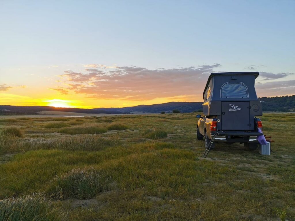 Cellule Billys installée sur un pick-up avec toit relevable, garée face au coucher de soleil dans un paysage de marais