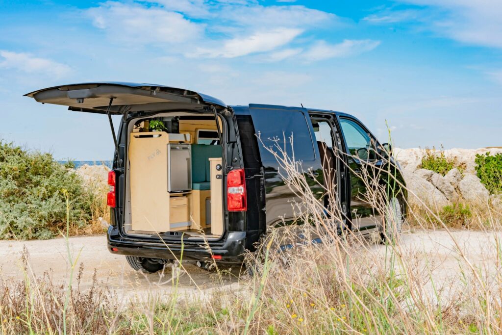 Module cuisine et rangement FLV Van en bois clair avec frigo intégré, installé à l'arrière d'un van au bord de mer